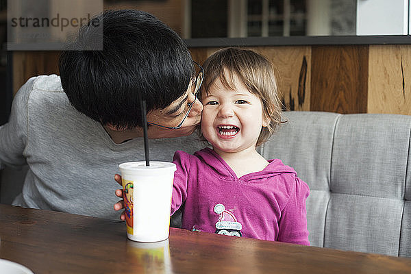 Vater küsst glückliche Tochter  während er im Café am Tisch sitzt