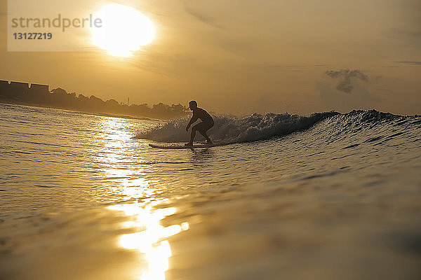 Scherenschnitt eines Mannes  der bei Sonnenuntergang in Bali auf dem Meer gegen den Himmel surft