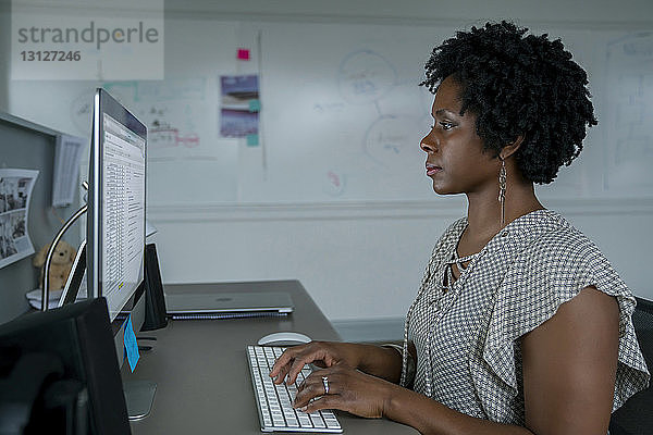 Seitenansicht einer Geschäftsfrau  die einen Desktop-Computer benutzt  während sie im Büro am Schreibtisch sitzt