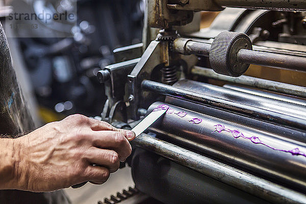Beschnittenes Bild einer Hand  die in einem Workshop violette Farbe auf eine Druckwalze aufträgt