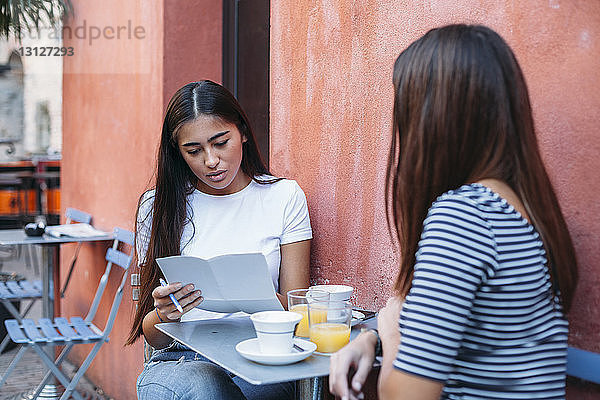 Frau liest Dokumente  während sie mit einem Freund im Straßencafé sitzt