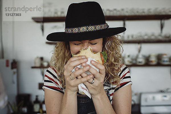 Nahaufnahme einer Frau mit Hut  die ein Sandwich hält  während sie zu Hause steht