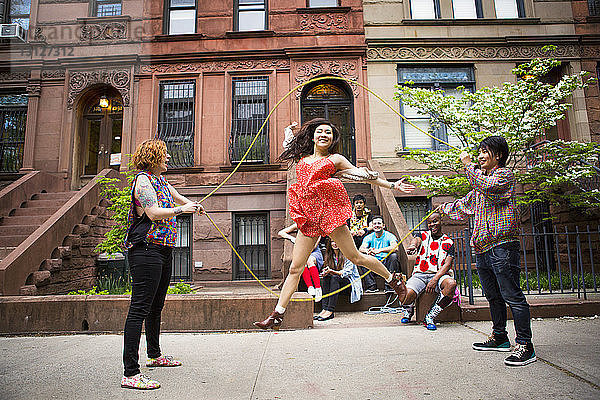 Freunde schauen auf Frau  die auf dem Bürgersteig gegen ein Gebäude Doppel-Holländisch spielt