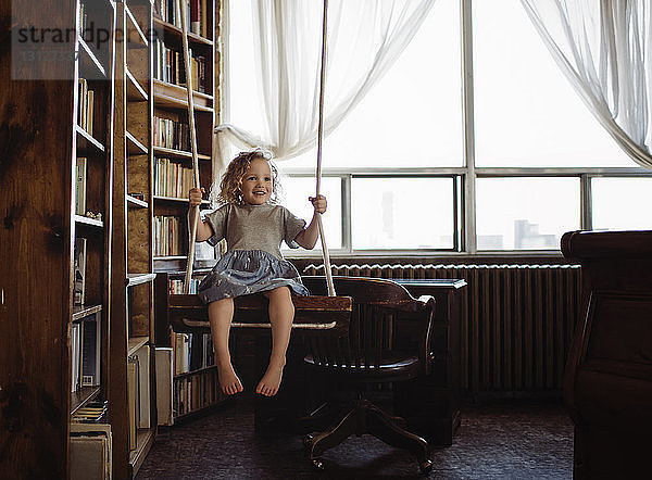 Glückliches Mädchen schaukelt zu Hause an Bücherregalen
