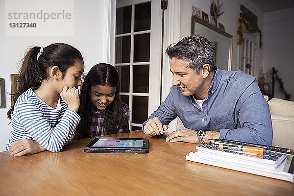 Vater und Töchter nutzen den Blick auf den Tablet-Computer  während sie am Tisch sitzen