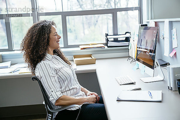 Seitenansicht einer lächelnden Geschäftsfrau  die auf einen Desktop-Computer im Büro schaut