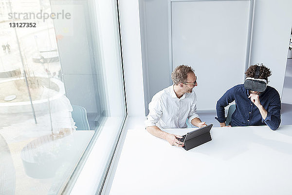 Ingenieur betrachtet männlichen Kollegen  der einen Virtual-Reality-Simulator im Büro untersucht