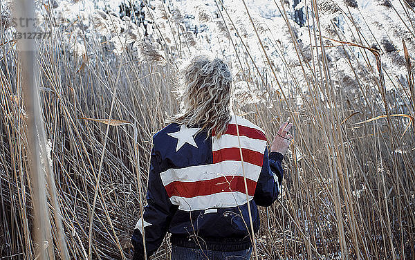 Rückansicht einer Frau  die eine Jacke mit amerikanischer Flagge trägt  während sie auf dem Feld inmitten von Pflanzen geht