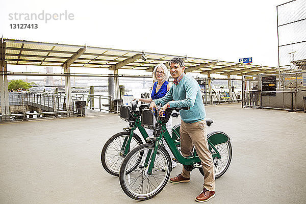Porträt eines glücklichen  reifen Paares  das mit Fahrrädern auf einem Fußweg steht