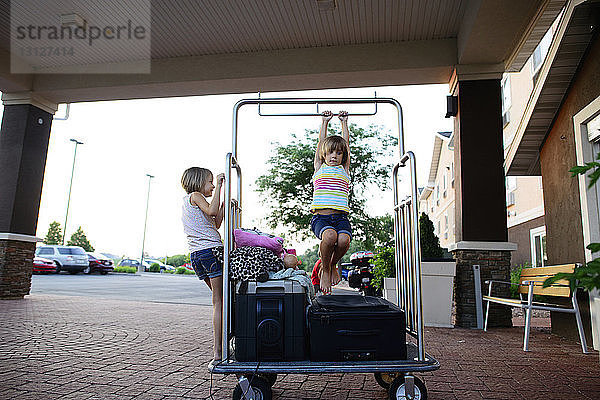 Schwestern spielen auf Gepäckwagen vor dem Hotel