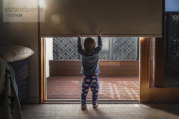 Rückansicht eines kleinen Mädchens mit erhobenen Armen am Eingang des Hauses stehend