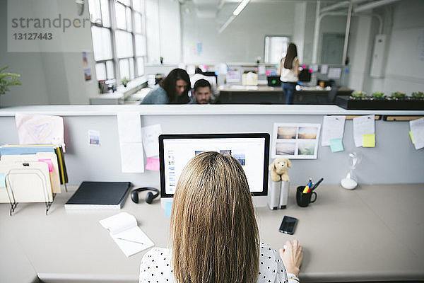 Rückansicht einer Geschäftsfrau am Desktop-Computer mit Kollegen im Hintergrund