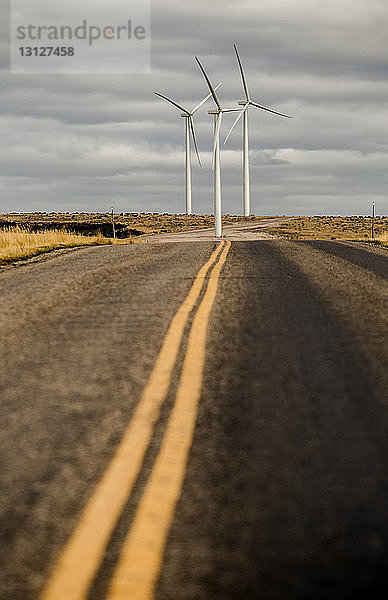 Straße führt zu Windmühlen gegen bewölkten Himmel am Bauernhof