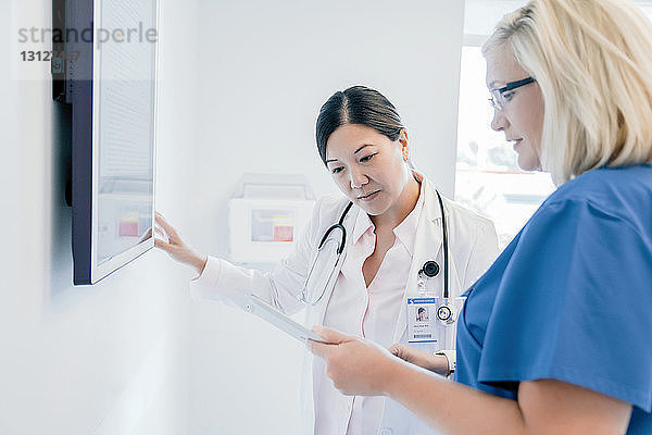 Ärztin zeigt im Krankenhaus stehend ihrer Kollegin einen Tablet-PC