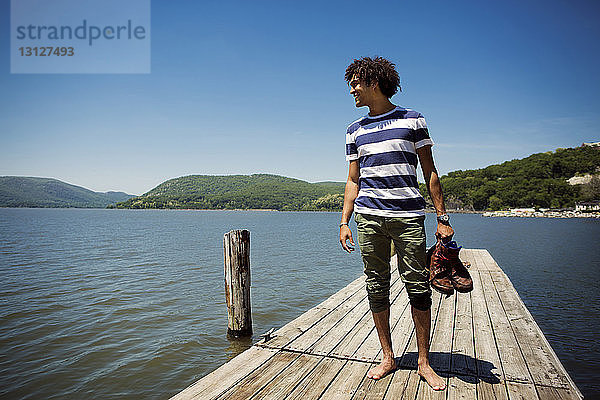 Lächelnder Mann mit Schuhen in der Hand  während er auf dem Steg über dem See steht