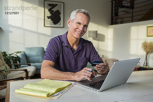 Porträt eines reifen Mannes  der einen Laptop-Computer benutzt  während er zu Hause Rechnungen bezahlt