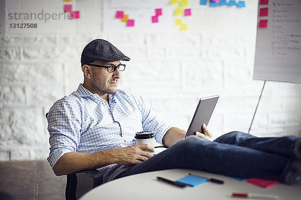 Selbstbewusster Geschäftsmann hält digitales Tablet  während er im Kreativbüro sitzt