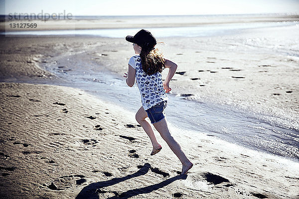 Verspieltes Mädchen rennt am Strand an einem sonnigen Tag