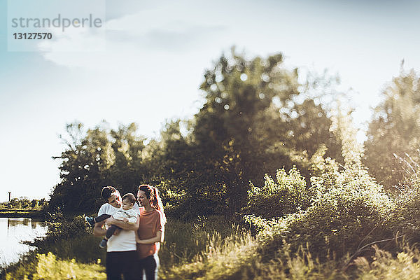 Glückliche Eltern mit Sohn am Seeufer vor bewölktem Himmel