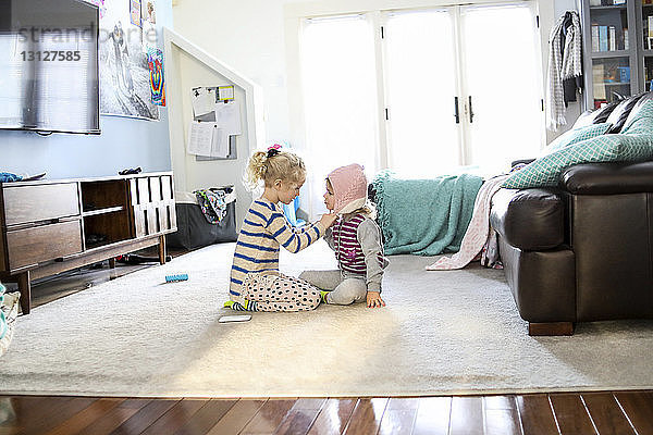 Seitenansicht eines Mädchens  das zu Hause im Wohnzimmer die Strickmütze seiner Schwester bindet