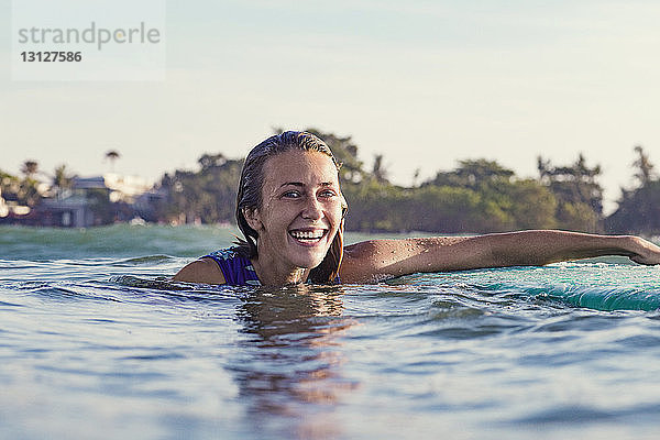Glückliche junge Frau schwimmt im Meer vor klarem Himmel