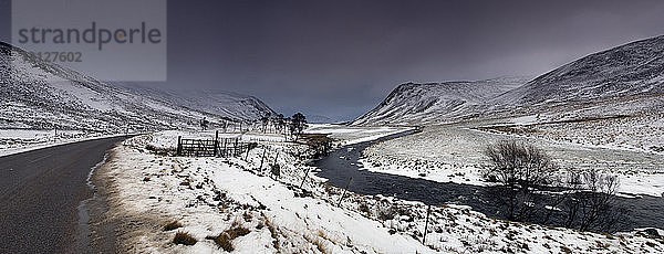 Panoramablick auf einen Bach  der an schneebedeckten Bergen vor bewölktem Himmel vorbeifließt