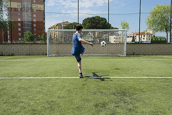 Rückansicht eines Jungen  der einen Fussball auf dem Feld in Richtung Netz kickt