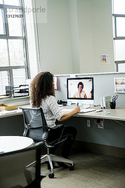Rückansicht der Videokonferenz einer Geschäftsfrau mit einer Kollegin über einen Desktop-Computer im Büro