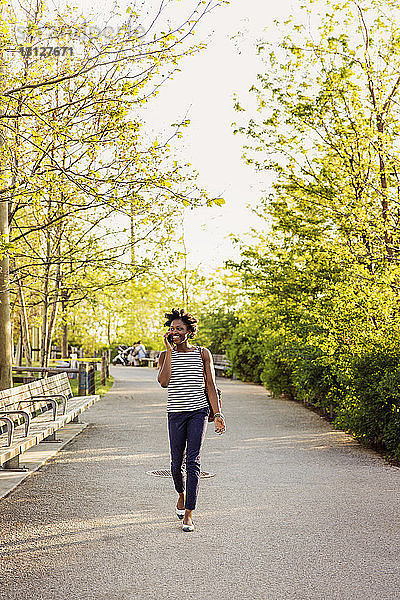 Glückliche Frau benutzt Smartphone  während sie auf einem Fußweg im Park spazieren geht
