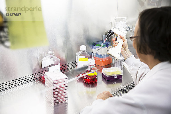Hochwinkelansicht einer leitenden Wissenschaftlerin mit einer Pipette während eines Experiments im Labor