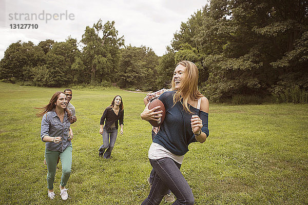 Spielerische Freunde jagen Frau  die auf einem Rasenplatz einen Fussball hält