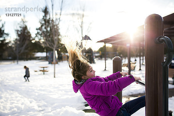 Mädchen spielt im Winter auf Holzkonstruktion im Park