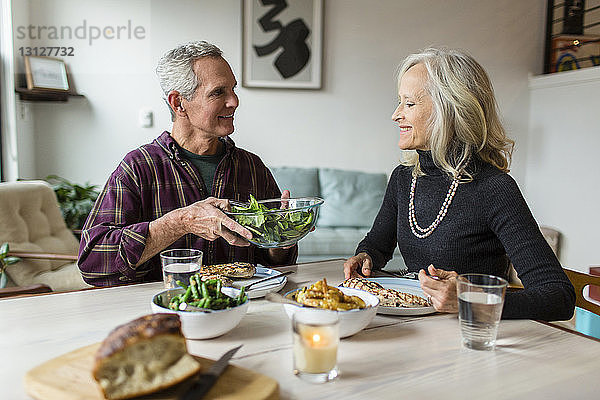 Lächelnder Mann schenkt Frau eine Schüssel Blattgemüse  während er am Esstisch sitzt