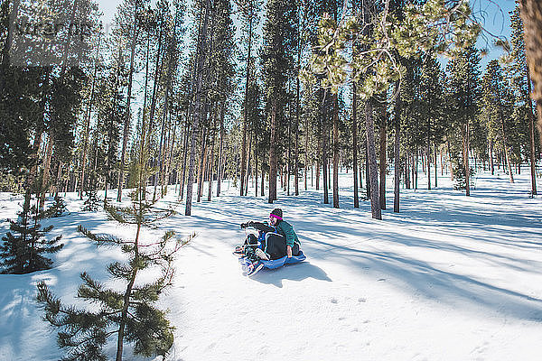 Mutter und Sohn rutschen auf schneebedecktem Feld gegen Bäume