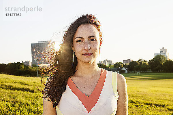 Porträt einer jungen Frau auf Grasfeld vor klarem Himmel