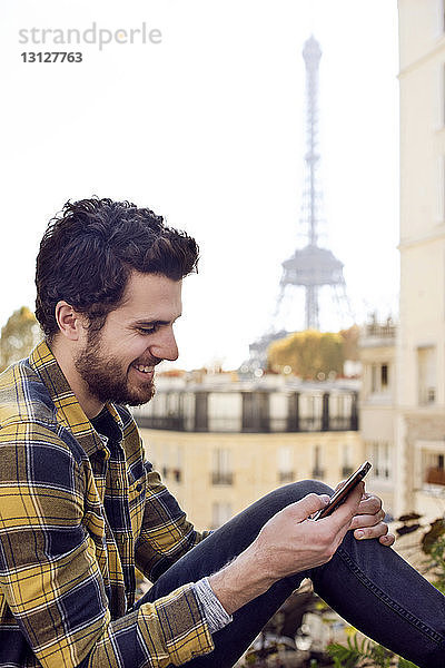 Lächelnder junger Mann mit Smartphone gegen Gebäude