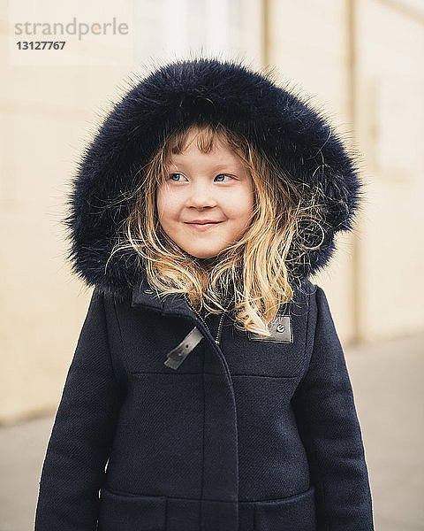 Lächelndes Mädchen schaut weg  während es draußen einen Pelzmantel trägt