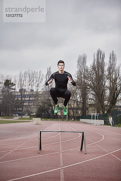 Porträt eines männlichen Athleten  der auf einer Sportbahn vor bewölktem Himmel trainiert