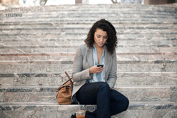 Geschäftsfrau benutzt ein Smartphone  während sie auf einer Treppe im Freien sitzt