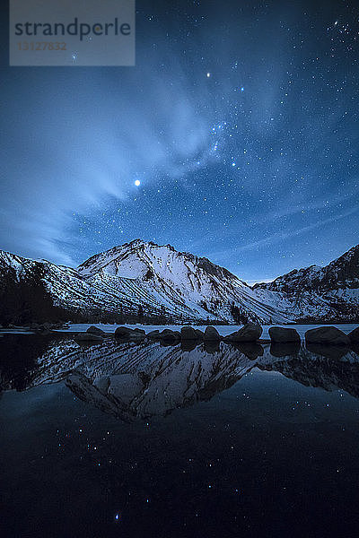 Blick auf den See bei schneebedecktem Berg vor Sternenhimmel