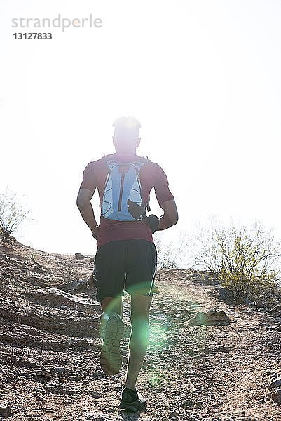 Rückansicht eines männlichen Wanderers mit Rucksack  der am sonnigen Tag auf dem Berg gegen den klaren Himmel läuft