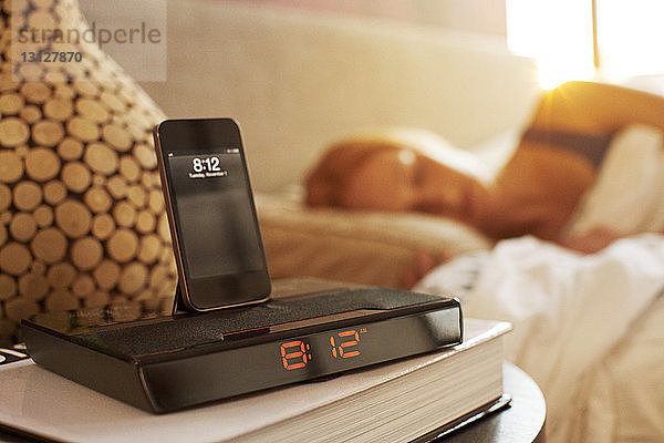 Smartphone auf modernem Wecker im Schlafzimmer