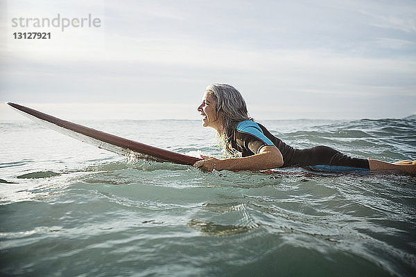 Seitenansicht einer glücklichen Surferin  die auf einem Surfbrett im Meer liegt