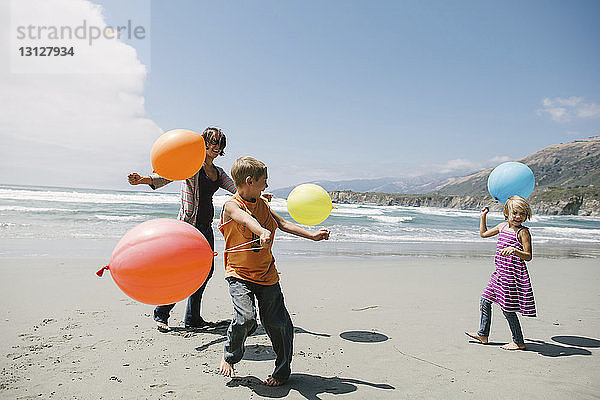 Fröhliche Familie spielt mit Luftballons  während sie am Strand im Sand steht