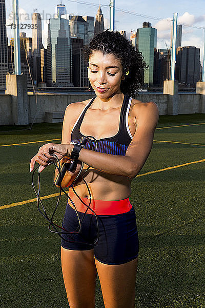 Sportlerin  die eine intelligente Uhr benutzt  während sie bei Sonnenuntergang auf einem Rasenfeld steht