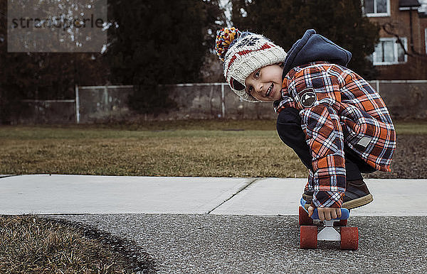 Porträt eines Skateboard fahrenden Jungen auf einem Fußweg im Park