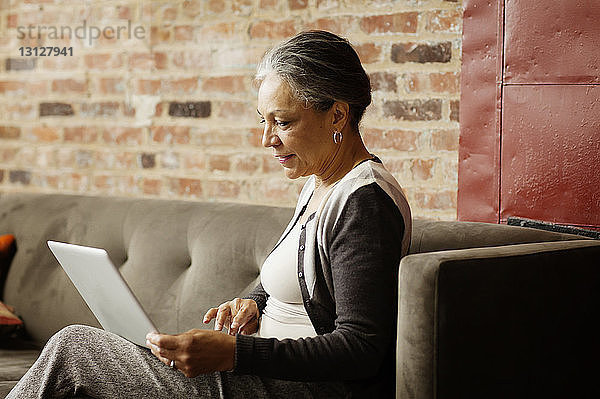 Seitenansicht einer Geschäftsfrau  die einen Laptop-Computer benutzt  während sie im Büro auf dem Sofa sitzt