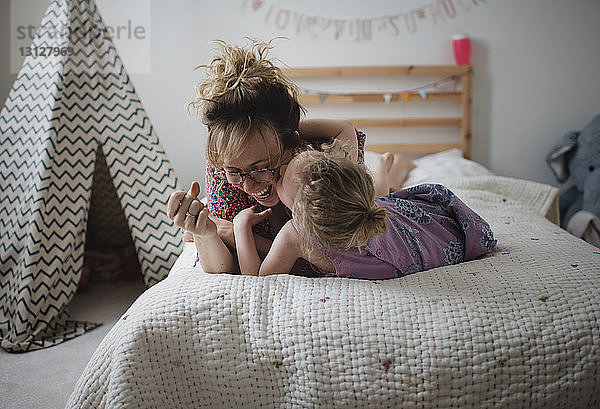 Tochter küsst glückliche Mutter  während sie zu Hause im Bett liegt