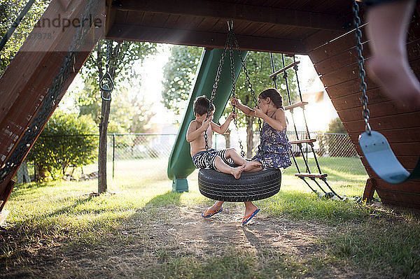 Verspielte Geschwister schaukeln auf der Reifenschaukel auf dem Spielplatz