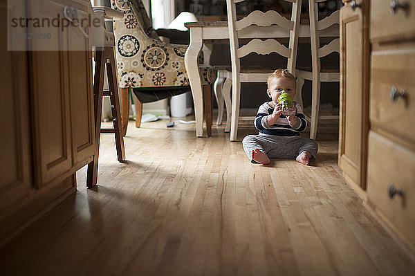 Porträt eines kleinen Jungen  der Wasser aus der Flasche trinkt  während er zu Hause auf dem Boden sitzt